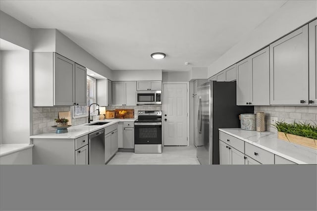 kitchen featuring a sink, stainless steel appliances, gray cabinetry, and decorative backsplash