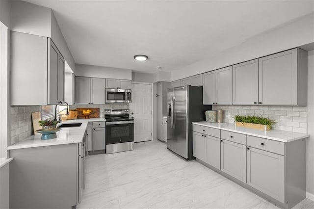 kitchen featuring decorative backsplash, gray cabinets, appliances with stainless steel finishes, and a sink