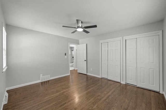 unfurnished bedroom with visible vents, two closets, baseboards, and wood finished floors