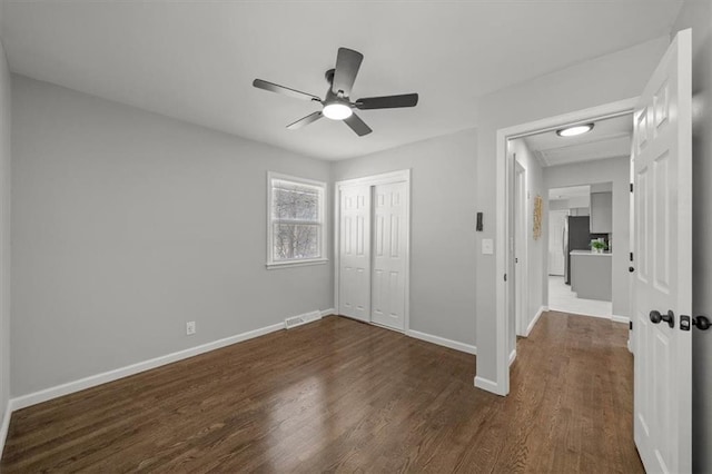 unfurnished bedroom with visible vents, dark wood finished floors, freestanding refrigerator, a closet, and baseboards