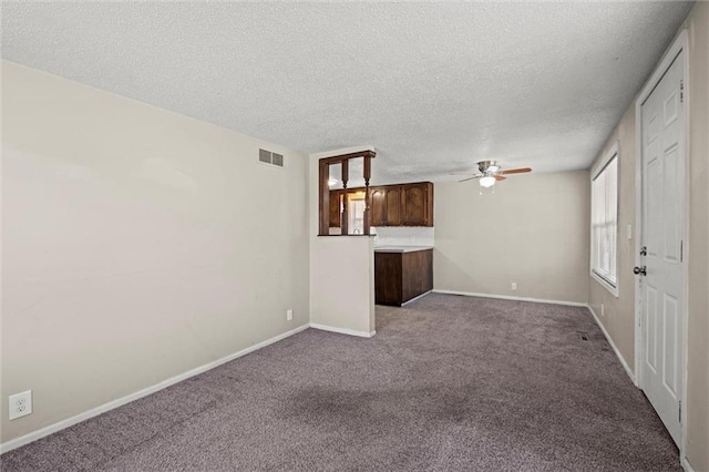 unfurnished living room with visible vents, a textured ceiling, dark carpet, baseboards, and ceiling fan