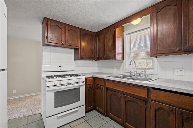 kitchen with light tile patterned flooring, light countertops, white range with gas stovetop, and a sink