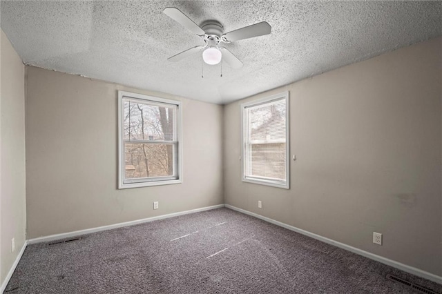 carpeted spare room featuring a healthy amount of sunlight, a textured ceiling, baseboards, and ceiling fan