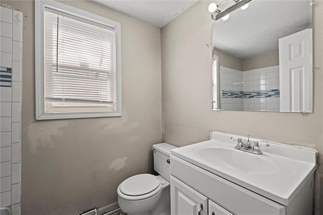 bathroom featuring a tile shower, a textured ceiling, toilet, and vanity