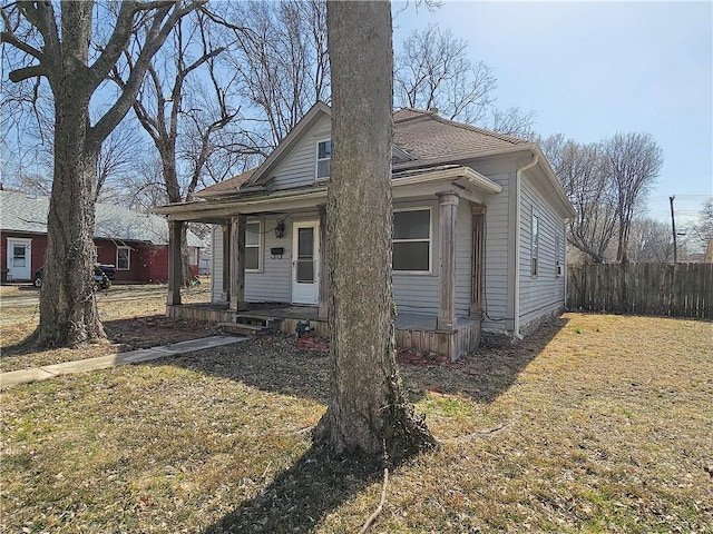 bungalow-style home with covered porch, a shingled roof, and fence