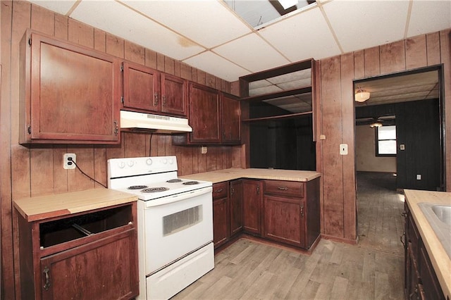 kitchen featuring light countertops, wood walls, under cabinet range hood, and white electric stove