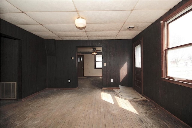 spare room with visible vents, a ceiling fan, wood-type flooring, wooden walls, and a paneled ceiling