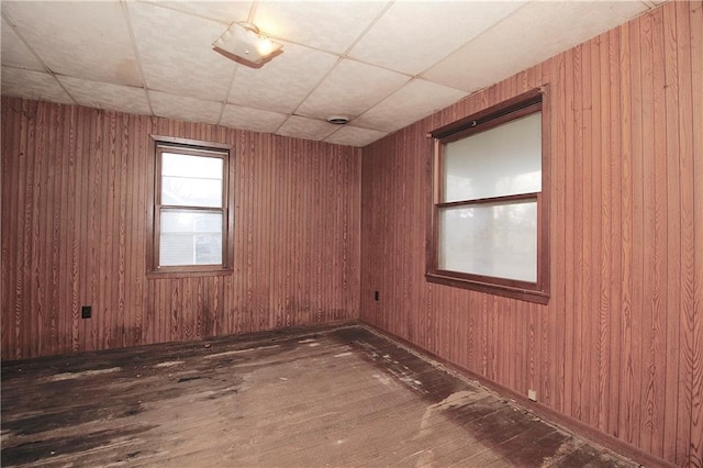 unfurnished room with a paneled ceiling, wood walls, and hardwood / wood-style flooring