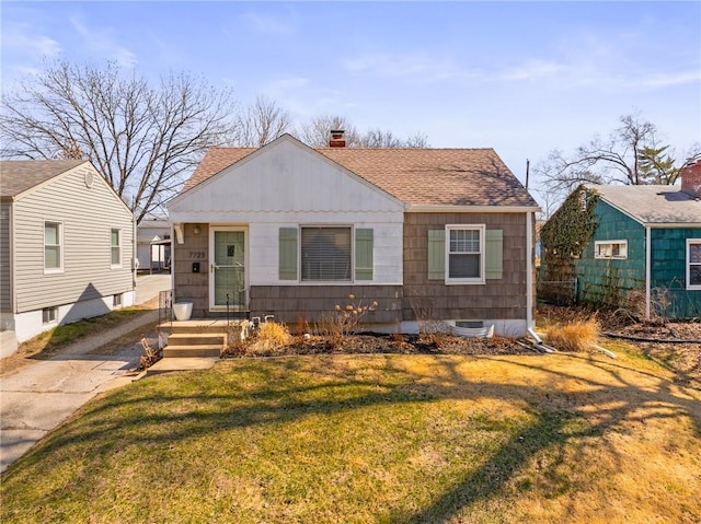 bungalow-style home featuring a chimney, roof with shingles, and a front yard