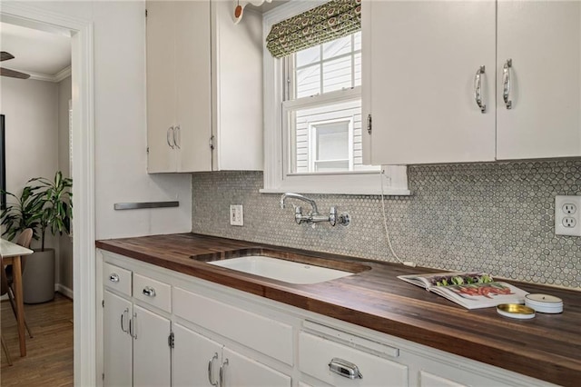 kitchen featuring a sink, backsplash, butcher block countertops, and white cabinets