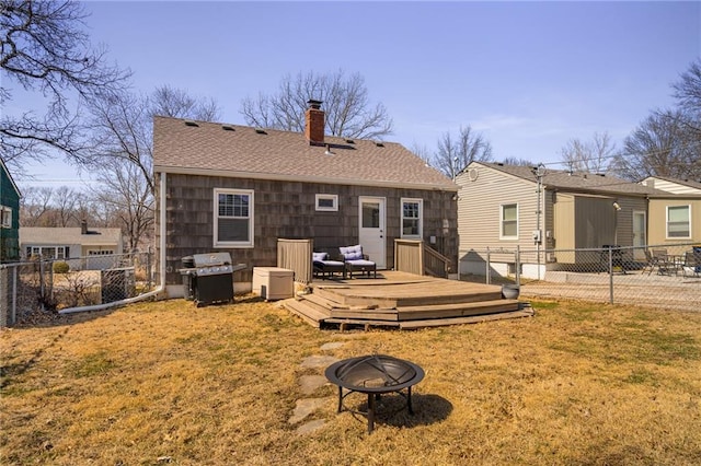 rear view of property featuring a fire pit, fence, a lawn, a chimney, and a deck