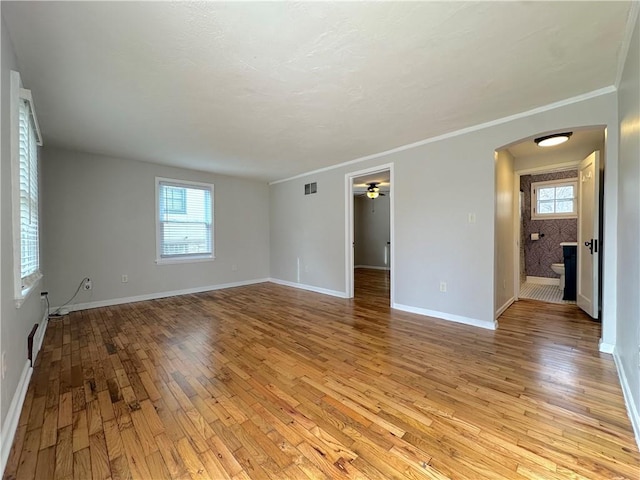 empty room featuring visible vents, baseboards, light wood-style flooring, arched walkways, and plenty of natural light