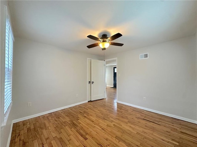 spare room featuring light wood-style flooring, a ceiling fan, visible vents, and baseboards