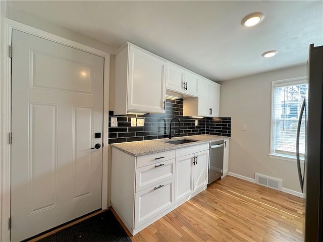 kitchen with visible vents, stainless steel appliances, a sink, light wood-style floors, and backsplash