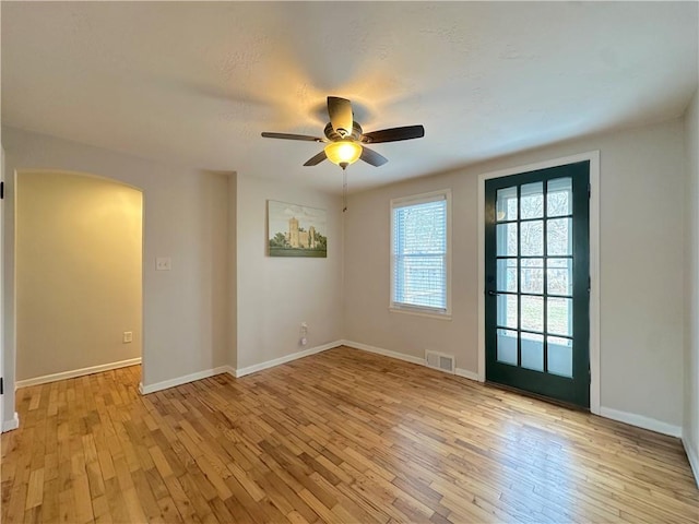 spare room featuring a ceiling fan, visible vents, baseboards, light wood-style flooring, and arched walkways