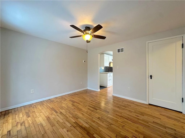 unfurnished room with light wood-type flooring, visible vents, a ceiling fan, arched walkways, and baseboards