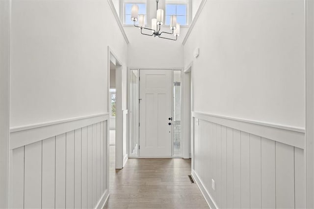 hallway featuring a chandelier, a wainscoted wall, visible vents, and wood finished floors