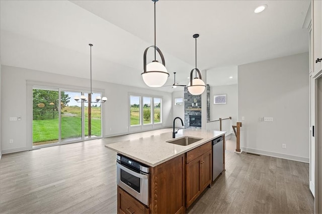 kitchen featuring a sink, a stone fireplace, light wood-style floors, appliances with stainless steel finishes, and open floor plan