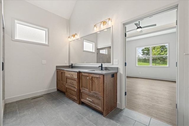 bathroom with ceiling fan, baseboards, lofted ceiling, double vanity, and a sink