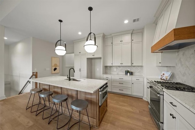22109 W 80th Ter, Shawnee, KS 66220 - kitchen with stainless steel appliances, premium range hood, light wood-style floors, tasteful backsplash, and a kitchen island with sink