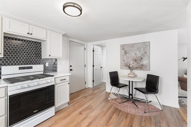 kitchen featuring white gas stove, light countertops, white cabinets, light wood-style floors, and tasteful backsplash