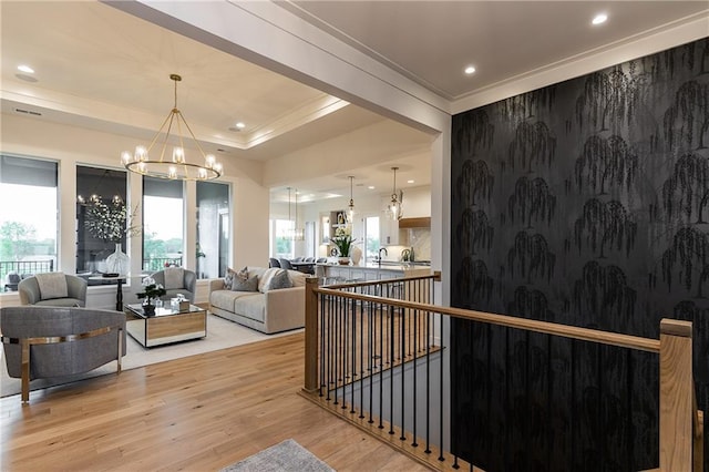 interior space with crown molding, light wood-type flooring, recessed lighting, a notable chandelier, and a raised ceiling