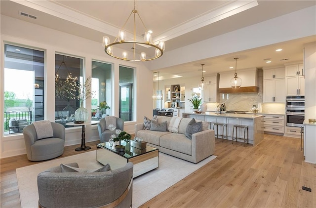 living area with light wood-style floors, visible vents, a notable chandelier, and ornamental molding