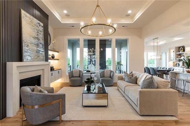 living area with a chandelier, a fireplace, light wood-type flooring, and a raised ceiling