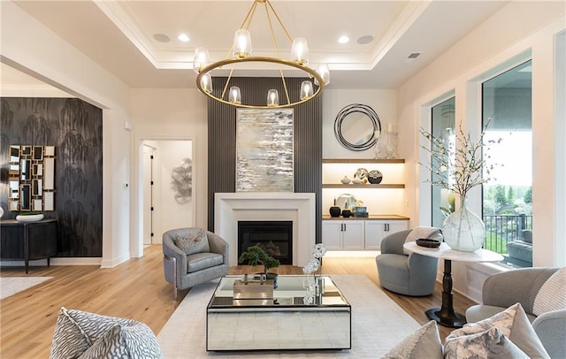 living room featuring an inviting chandelier, a fireplace, a tray ceiling, and wood finished floors