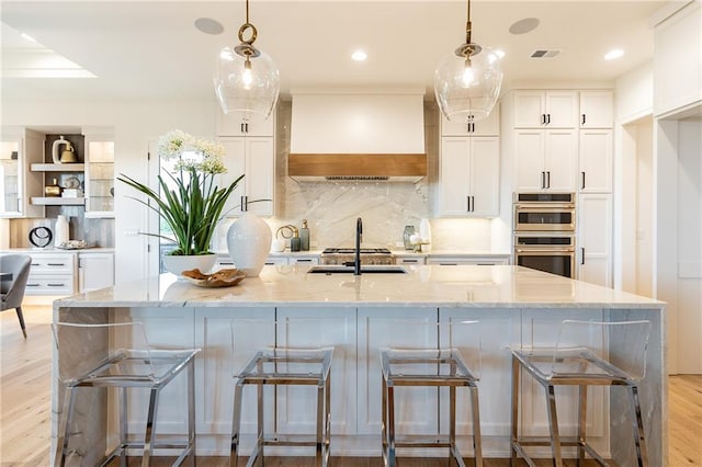 kitchen with light wood finished floors, visible vents, premium range hood, double oven, and white cabinets