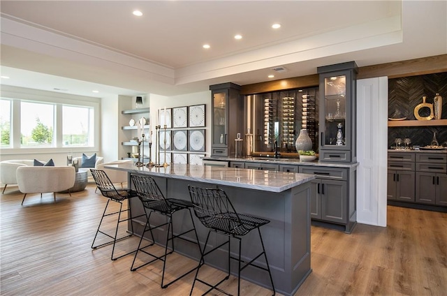 kitchen featuring gray cabinetry, a breakfast bar area, light wood-type flooring, and light stone countertops