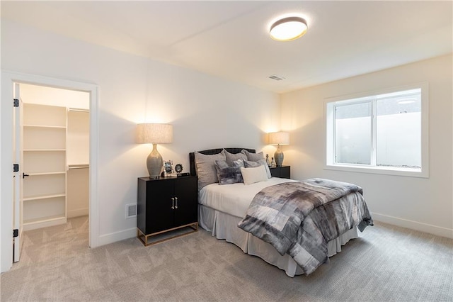 bedroom with light carpet, visible vents, a walk in closet, and baseboards