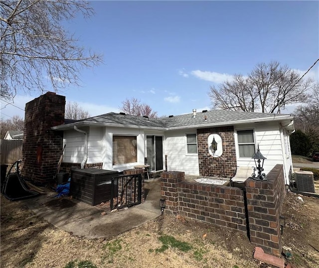 rear view of house featuring a patio, roof with shingles, central AC, and a chimney