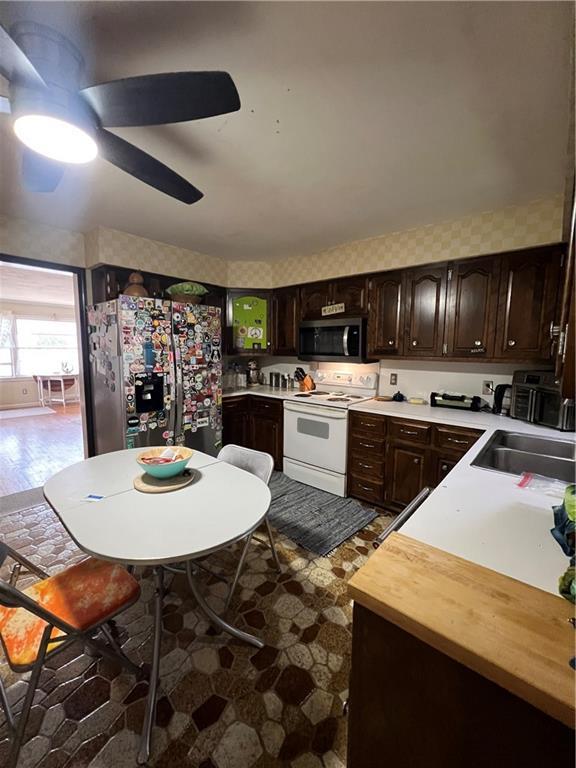 kitchen with dark brown cabinets, wallpapered walls, ceiling fan, stainless steel appliances, and a sink