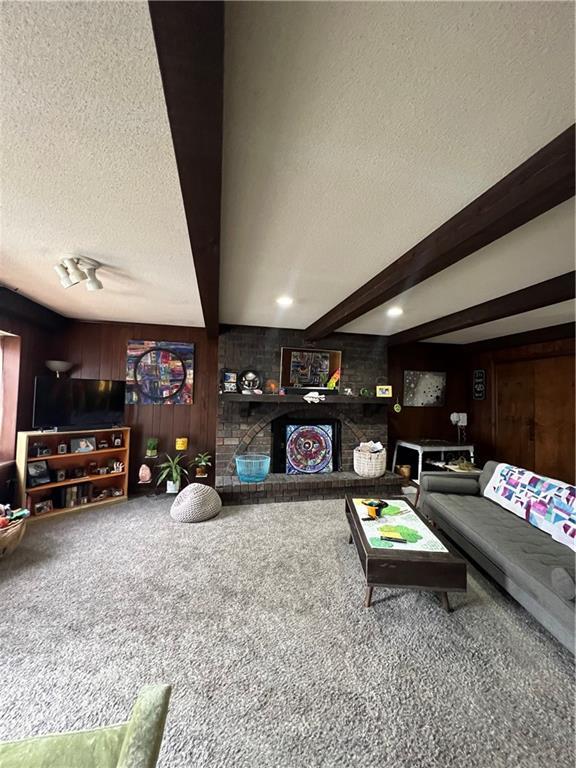 carpeted living room featuring beamed ceiling, a textured ceiling, and wood walls