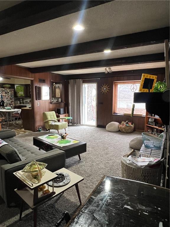 carpeted living room with beam ceiling, a textured ceiling, and wood walls