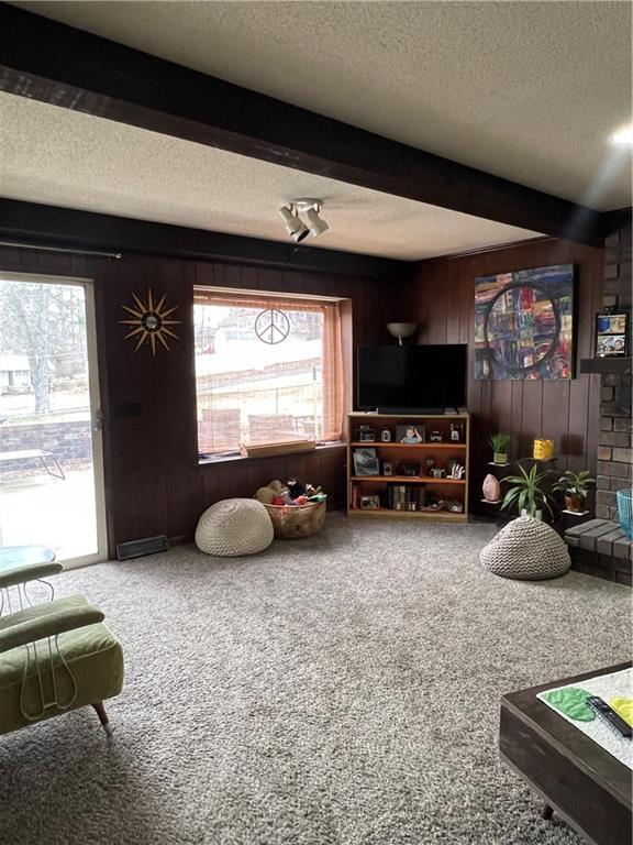 living area with beam ceiling, carpet flooring, wood walls, and a textured ceiling