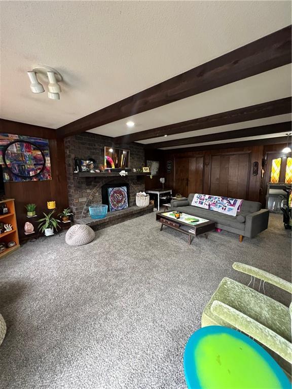 carpeted living area with beamed ceiling, a textured ceiling, and wood walls