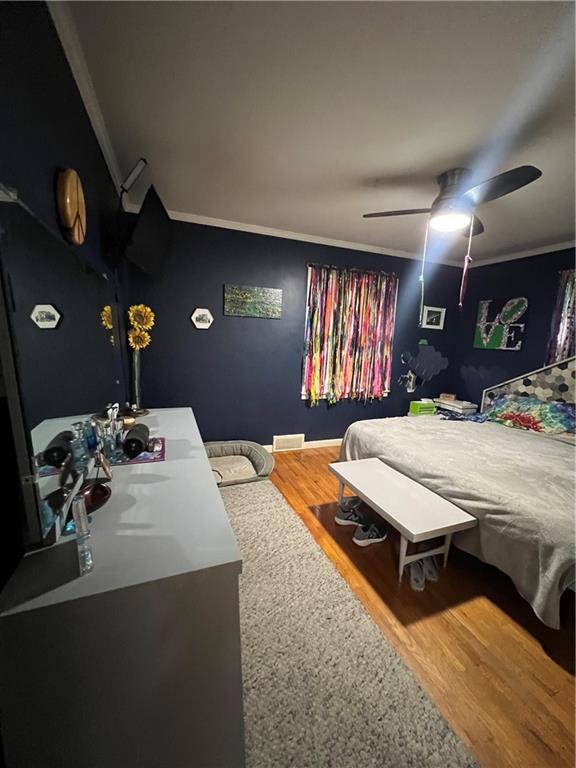 bedroom with wood finished floors, a ceiling fan, and ornamental molding