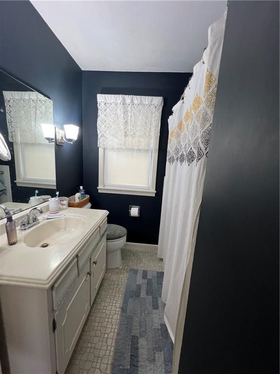 bathroom featuring a shower with shower curtain, baseboards, toilet, and vanity