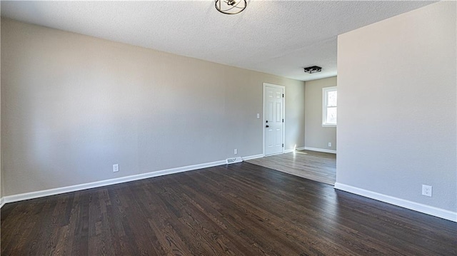 spare room featuring visible vents, a textured ceiling, baseboards, and dark wood-style flooring