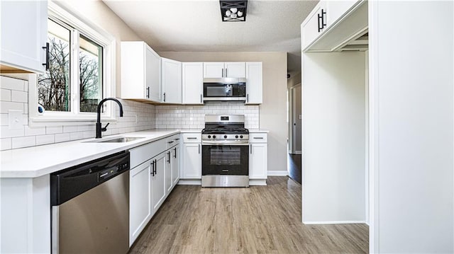 kitchen featuring decorative backsplash, stainless steel appliances, light wood-style floors, white cabinetry, and a sink