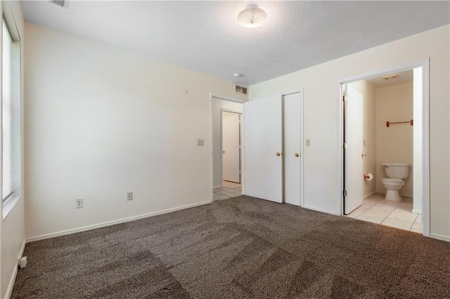 unfurnished bedroom featuring visible vents, ensuite bathroom, a closet, baseboards, and light colored carpet