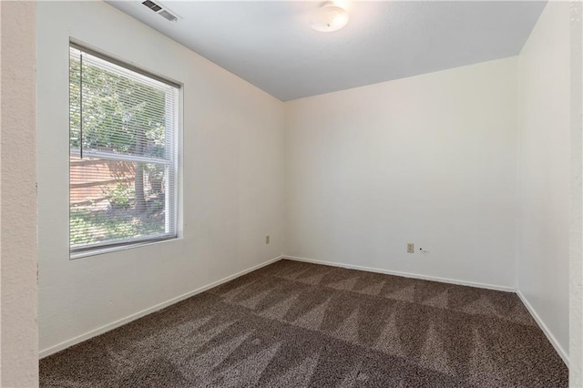 spare room with baseboards, visible vents, and dark colored carpet