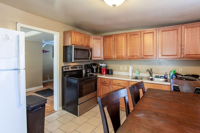 kitchen with light tile patterned floors, baseboards, a sink, light countertops, and appliances with stainless steel finishes