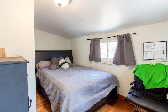 bedroom featuring baseboards, wood finished floors, and vaulted ceiling