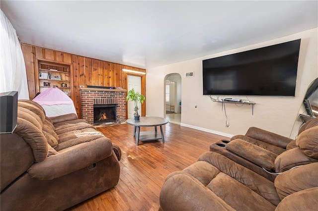 living room featuring hardwood / wood-style floors, visible vents, baseboards, arched walkways, and a brick fireplace