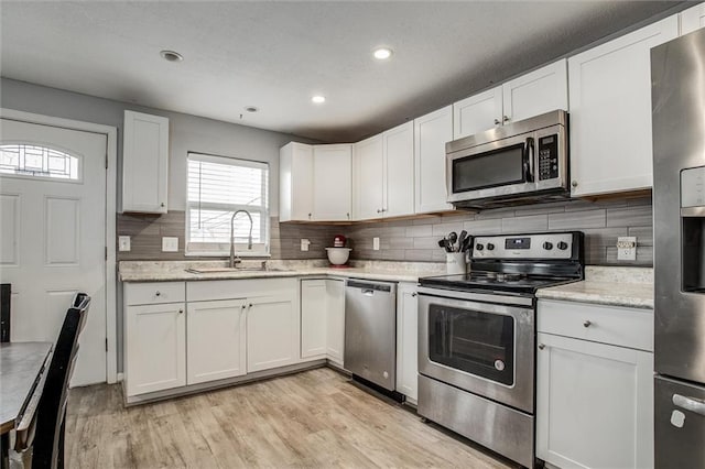 kitchen featuring light wood finished floors, tasteful backsplash, appliances with stainless steel finishes, white cabinets, and a sink