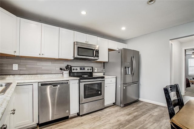 kitchen with light wood-type flooring, tasteful backsplash, stainless steel appliances, white cabinets, and light countertops