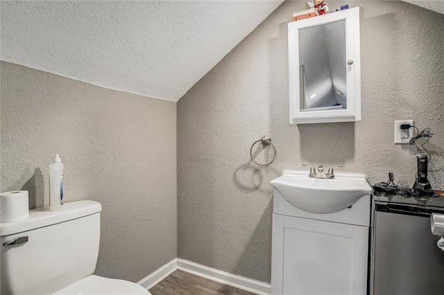 half bathroom featuring toilet, wood finished floors, vanity, and a textured wall